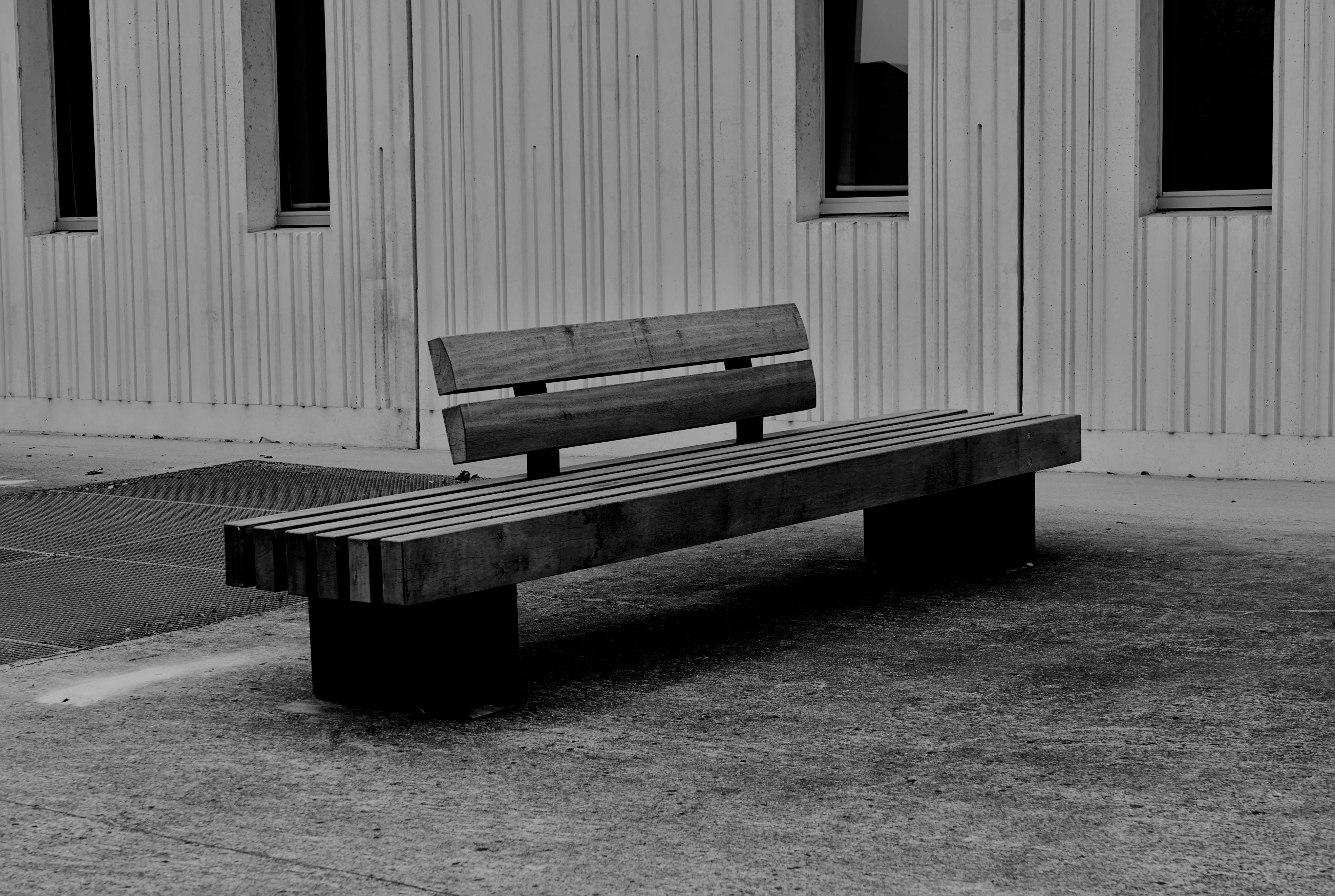 Black and white photo of a modern wooden bench outside a building facade.