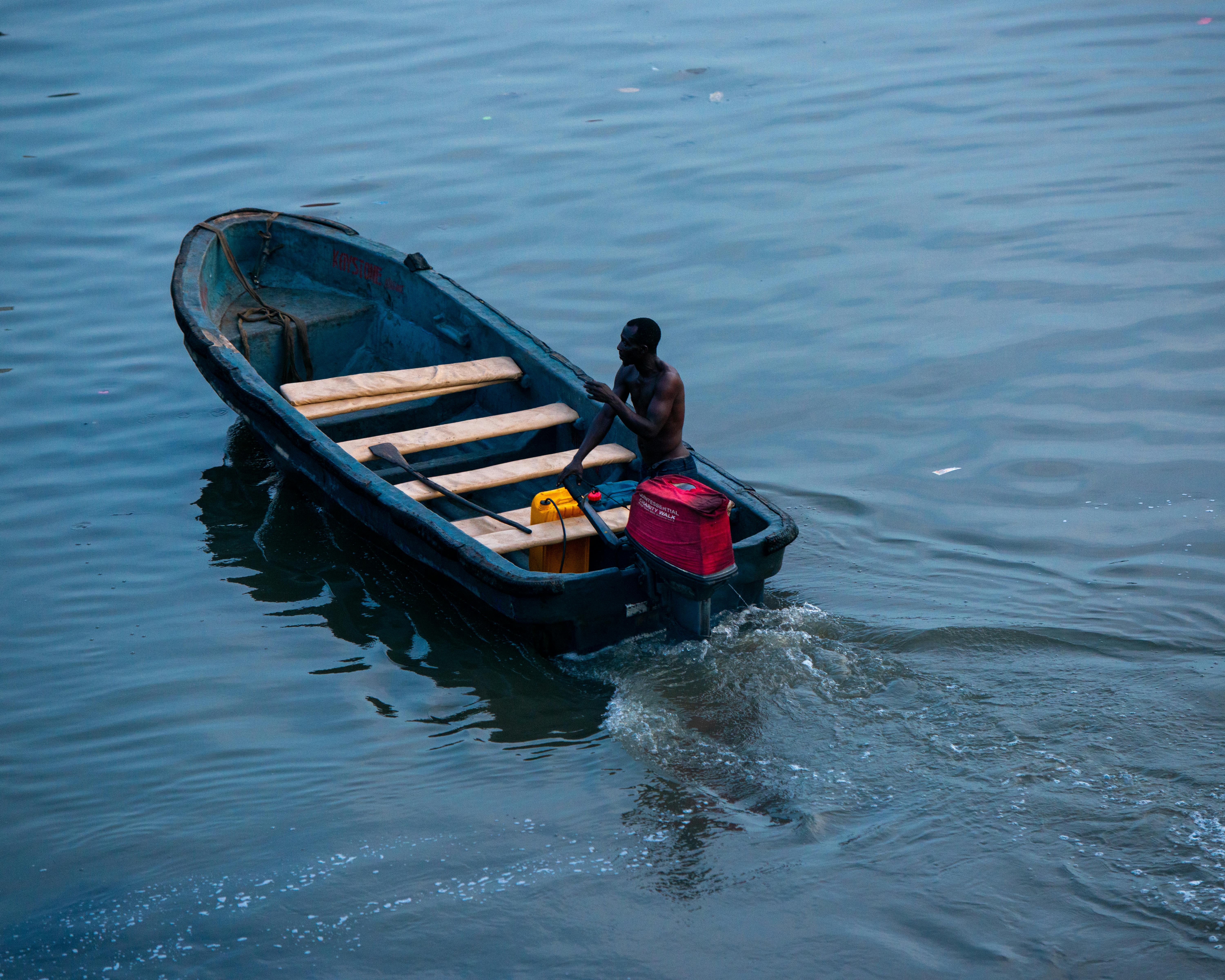 Free A lone fisherman maneuvers his canoe across calm waters in Lagos, Nigeria during blue hour. Stock Photo