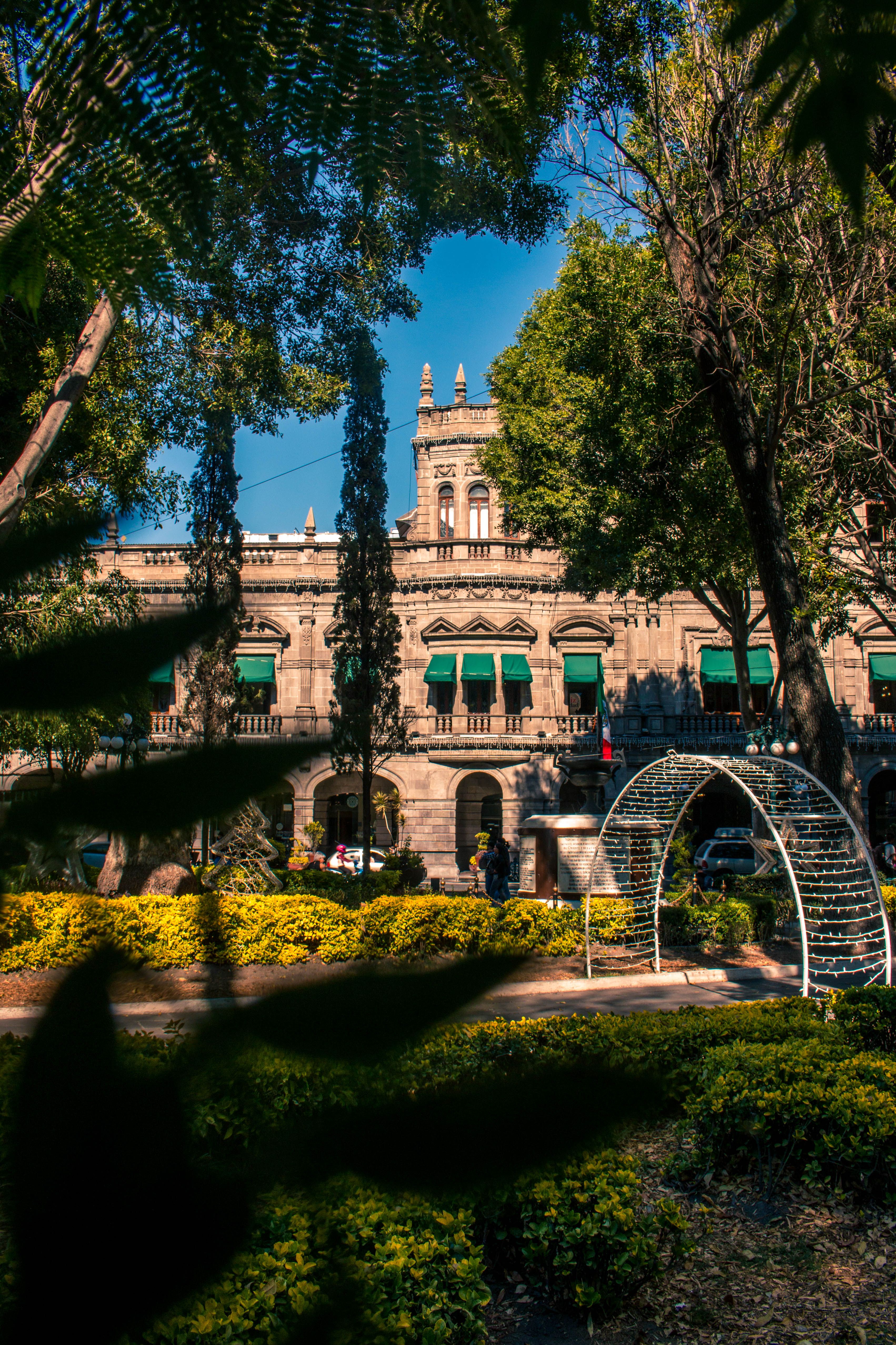 Beautiful sunlit view of a historic building in Puebla, Mexico, framed by lush park foliage.