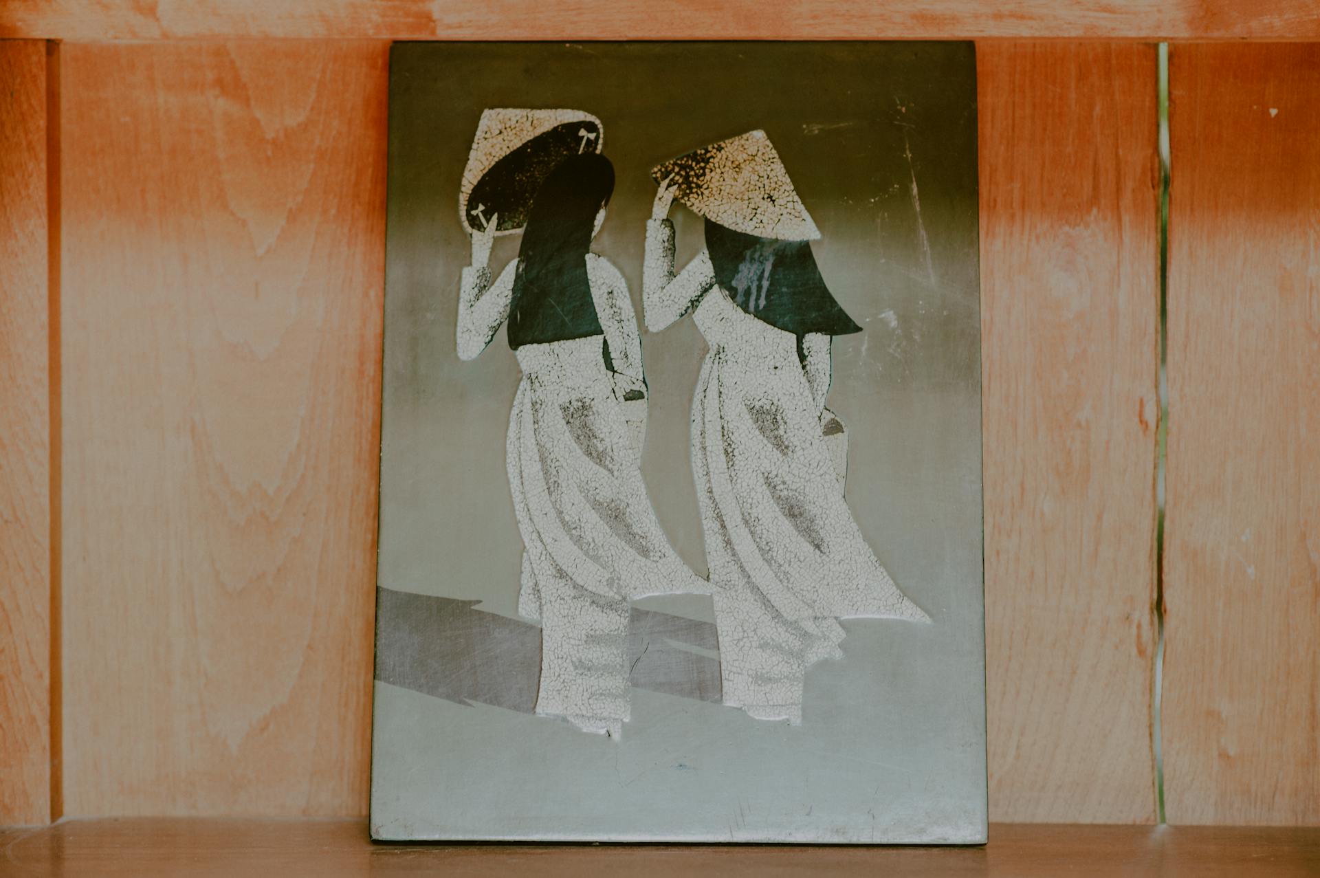 Elegant traditional wall art depicting two figures in cultural attire on a wooden background.