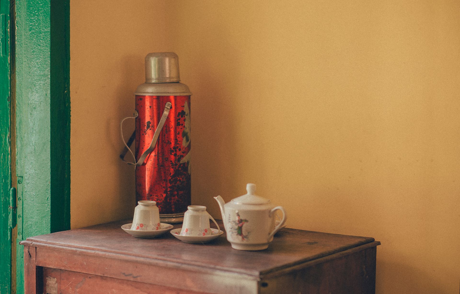Retro setup of teapot and cups with a thermos on a wooden table in a cozy indoor setting.