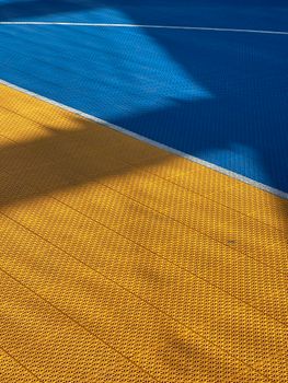 Close-up of a vivid blue and yellow sports court with geometric patterns and shadows.