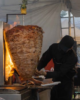 A street vendor prepares shawarma on a flaming vertical spit at an outdoor market.