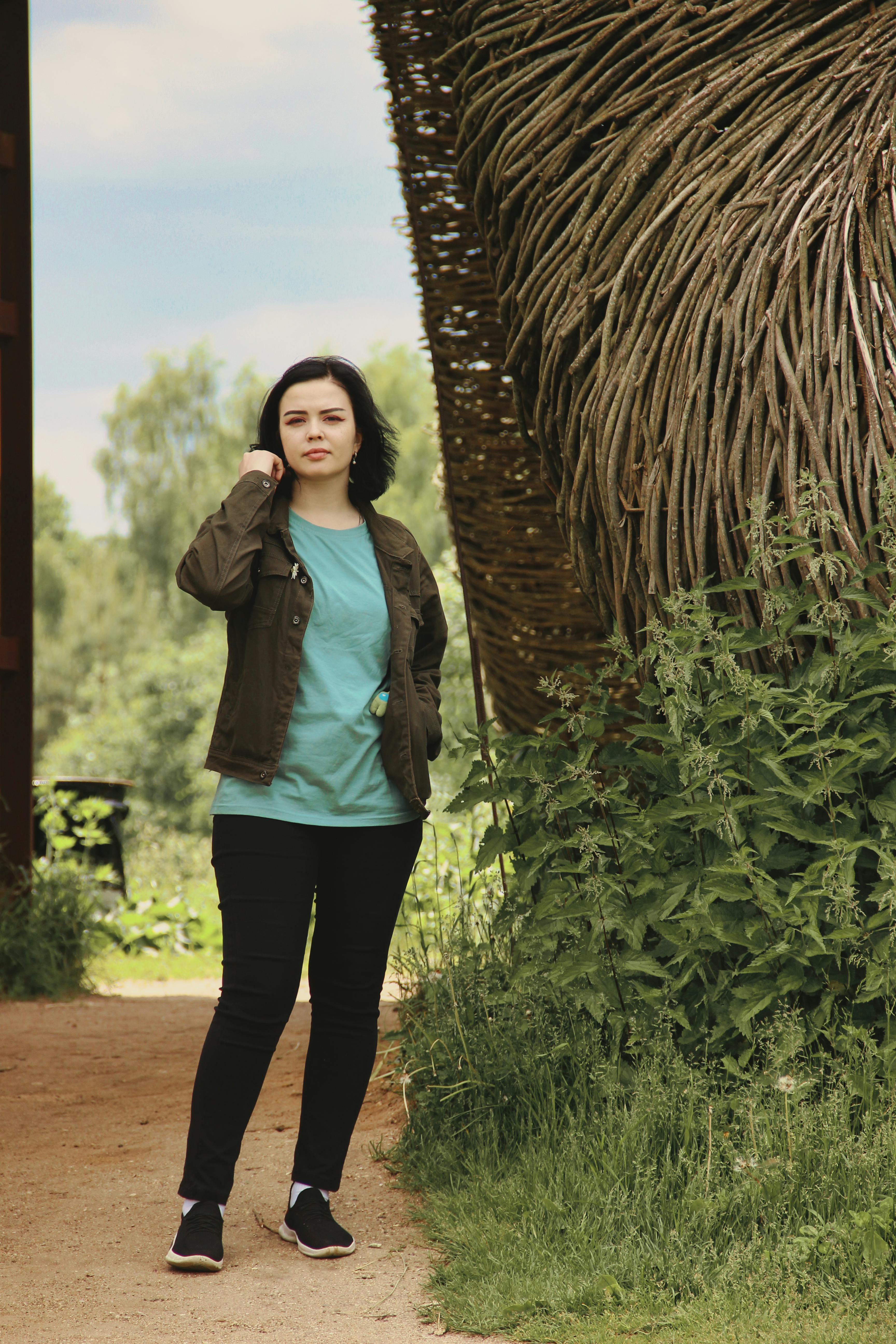 Casual portrait of a young woman outdoors in a rustic setting amidst greenery.