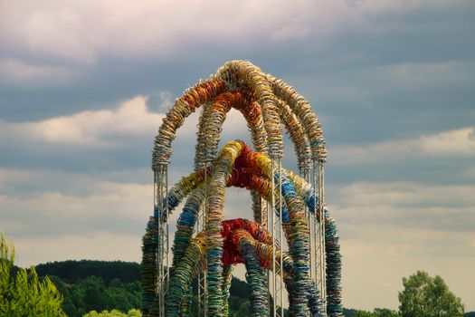 A striking outdoor sculpture made from colorful bicycle wheels against a lush, cloudy backdrop.