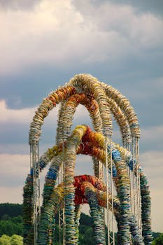 A dynamic art structure made of recycled materials set against a dramatic cloudy sky backdrop.