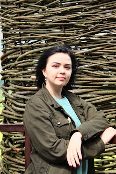 Young woman posing outdoors against a rustic woven wooden backdrop.