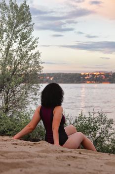 A woman in a swimsuit enjoys a peaceful sunset by the river, surrounded by nature.