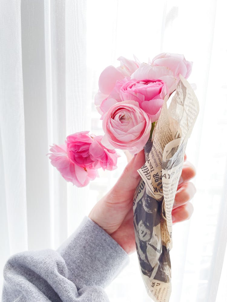 Woman Hand Holding Peonies Bouquet Wrapped In Newspaper