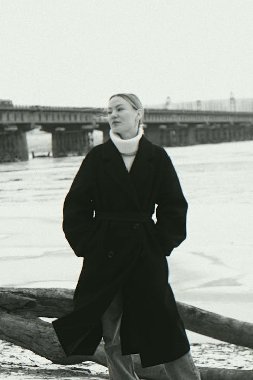 Young Woman in Coat Standing on River Bank