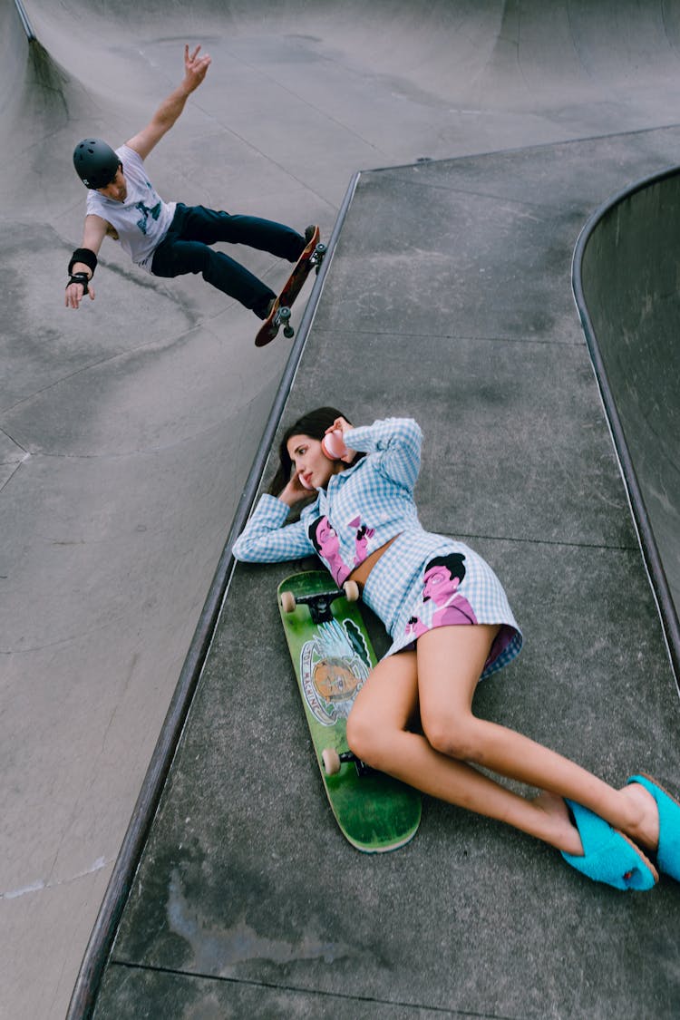 Woman Lying Down On Wall And Man Skating In Skatepark