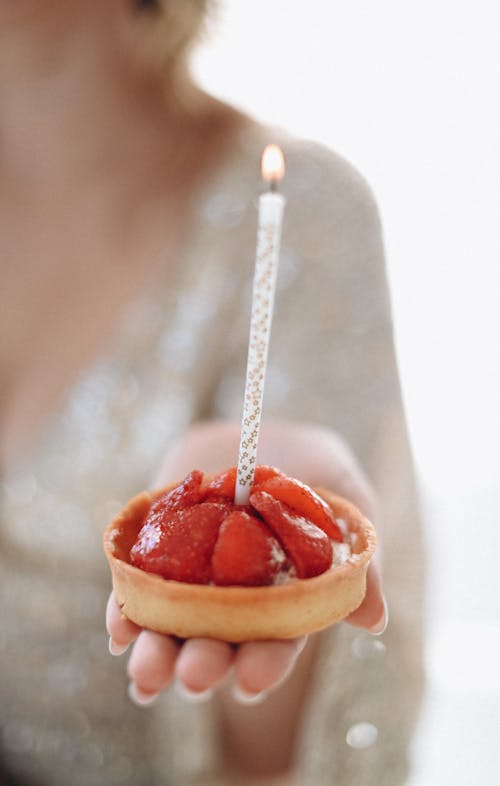 Hand of a Woman Holding a Small Strawberry Cake with a Burning Candle