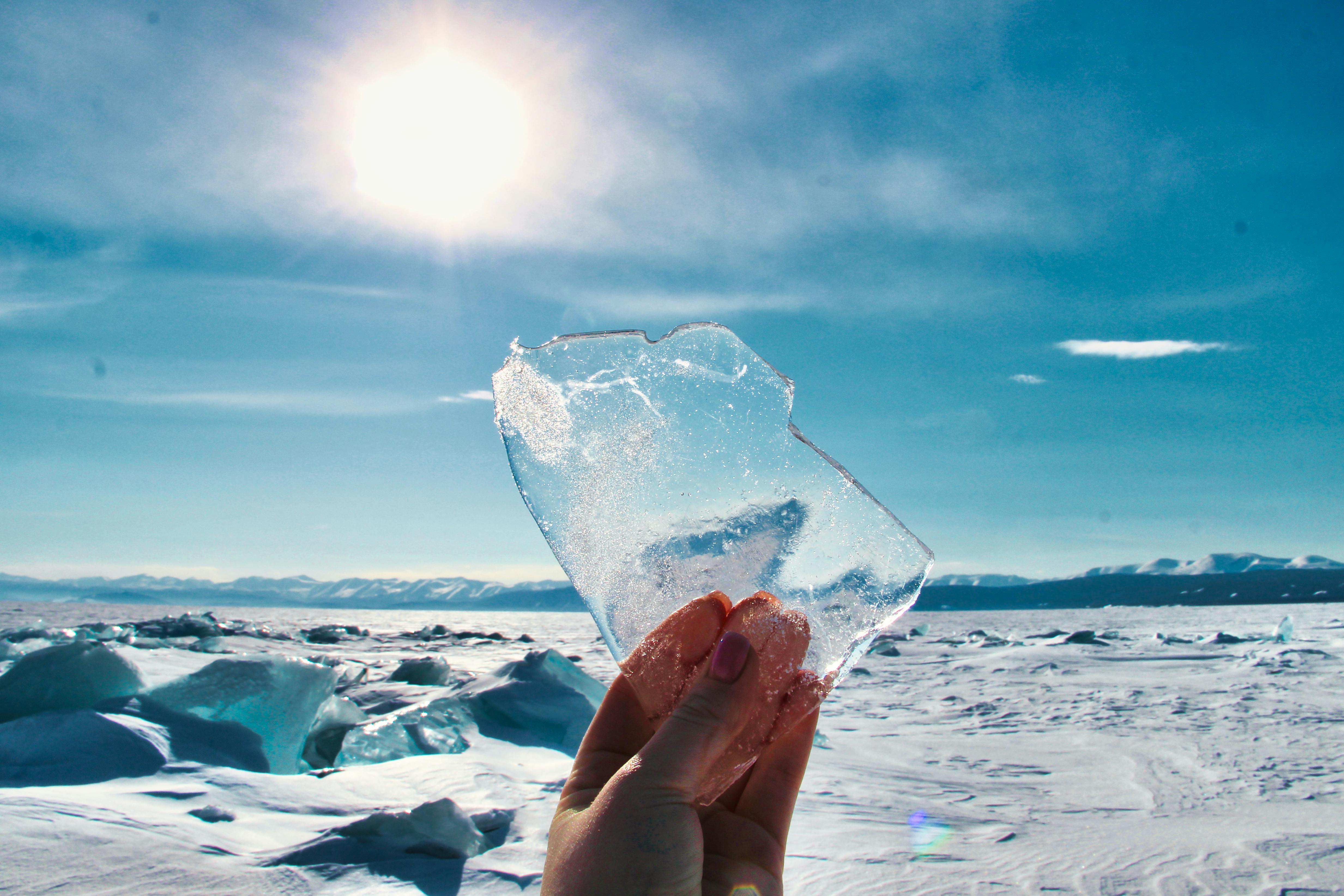 a person holding up a piece of ice in front of the sun