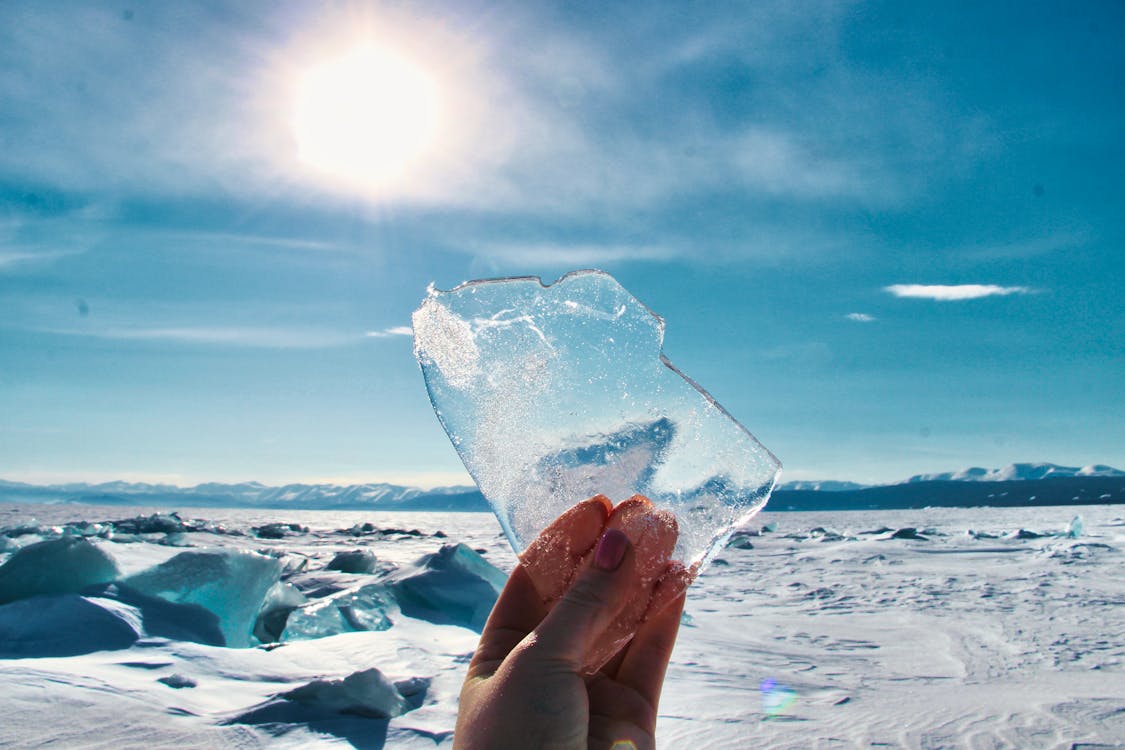 A person holding up a piece of ice in front of the sun