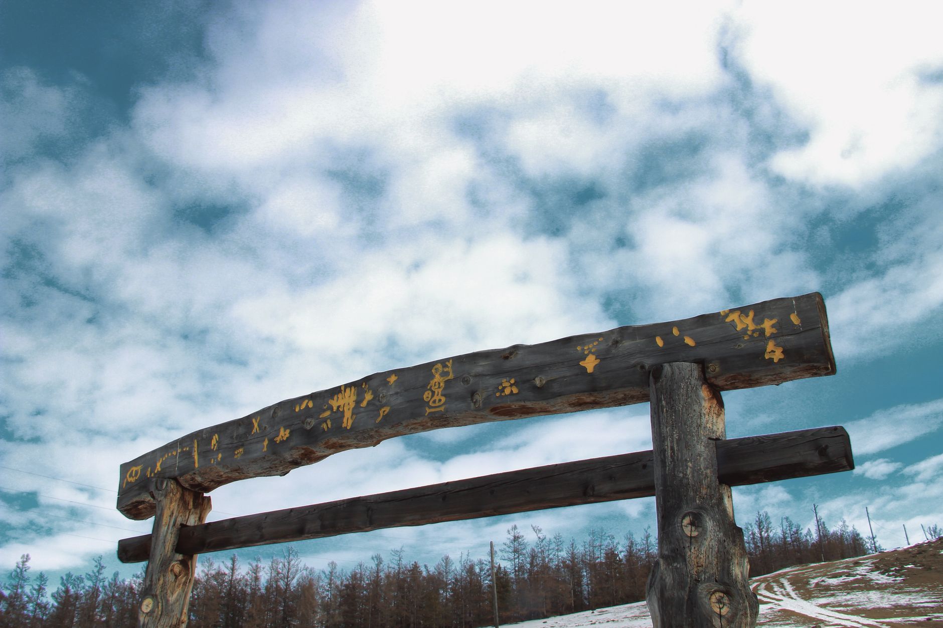 A rustic wooden archway stands prominent against a cloudy winter sky with snow and sparse forest.