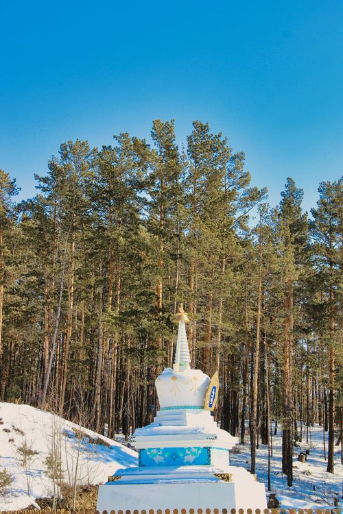 Free A white stupa stands amidst tall trees and snow under a clear blue sky. Stock Photo