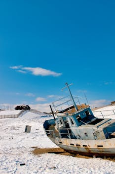 A rusted boat rests on a snowy landscape, under clear blue skies, depicting solitude and abandonment.