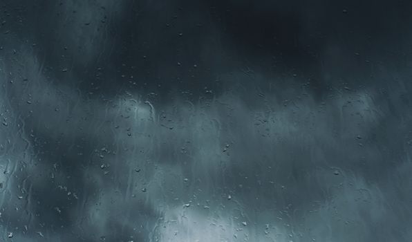 Moody image of rain streaming down a window with dark storm clouds overhead.