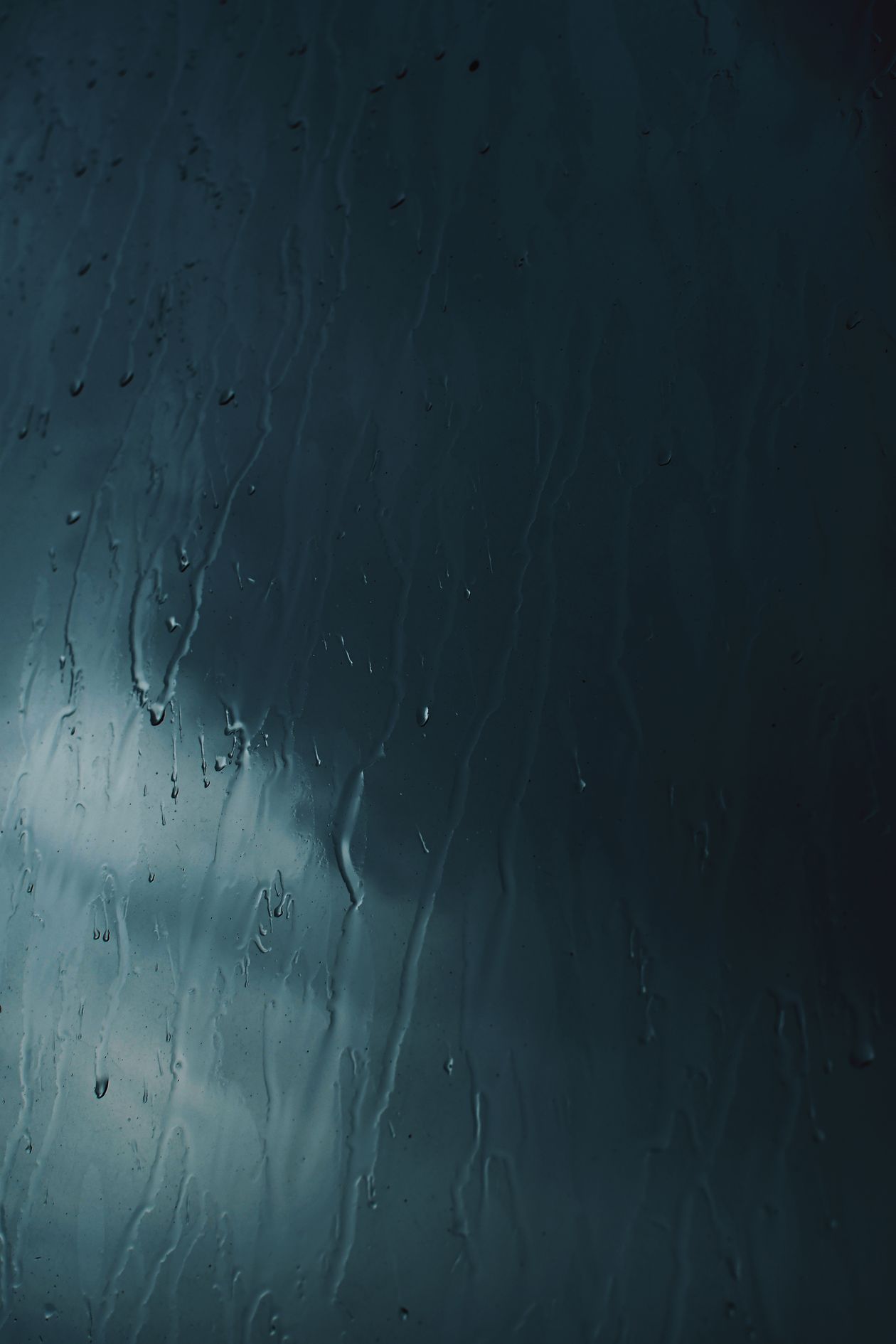 Rain running down a window under a dark sky