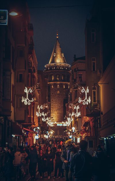 A busy city street at night beneath a lit stone tower — photo by Firat Oter on Pexels