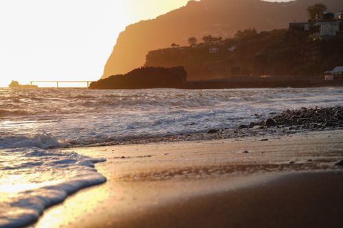Free Breathtaking sunset over a rocky beach with gentle waves against a mountain backdrop. Stock Photo