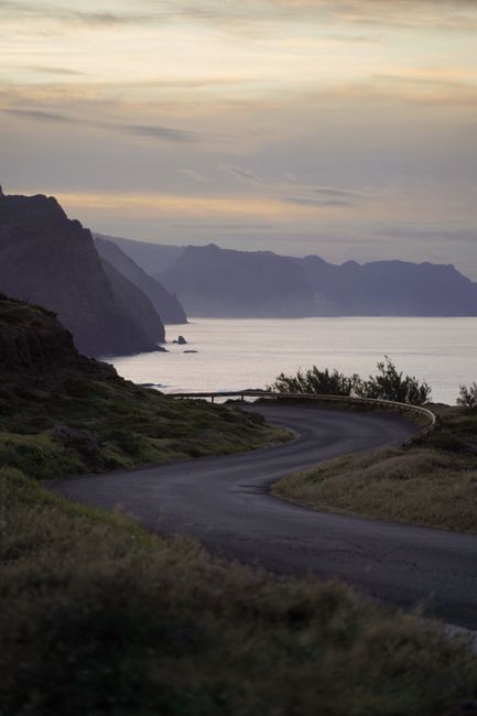 A winding road by the coast with mountains and sea under a sunset sky, perfect for travel inspiration.