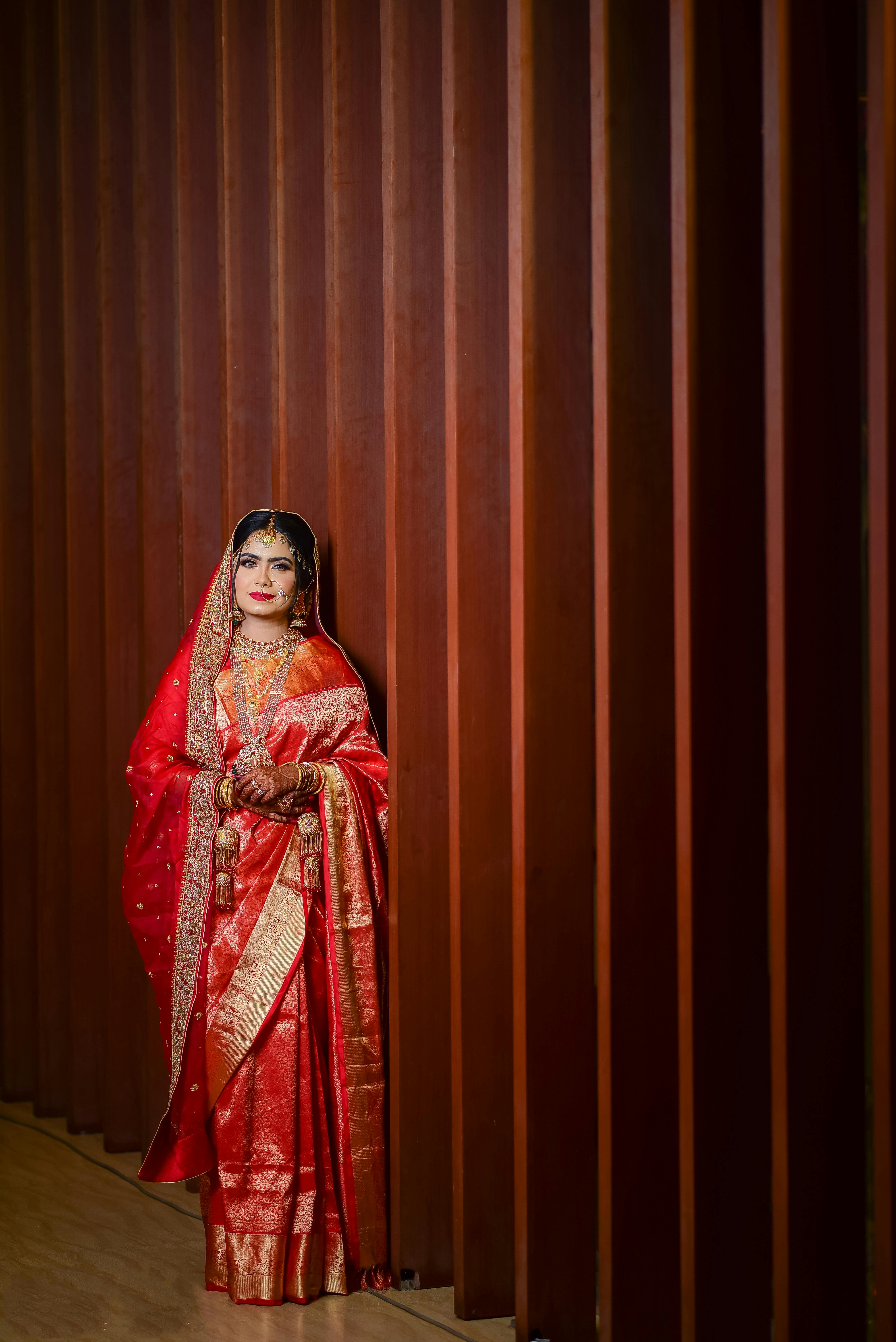 Portrait of a South Asian woman in a vibrant red sari, standing gracefully indoors.