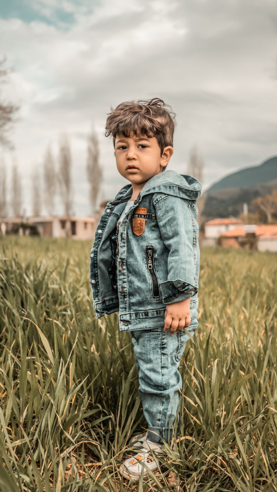 Boy in a denim outfit standing in a grassy field