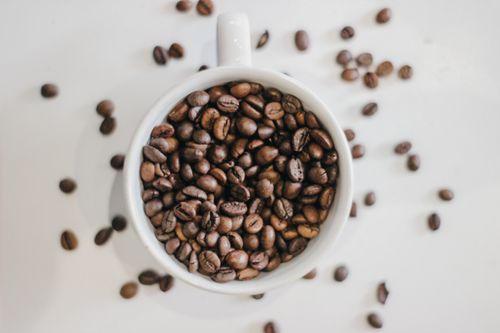 Free Aerial view of coffee beans filling a white mug with scattered beans on a white surface. Stock Photo
