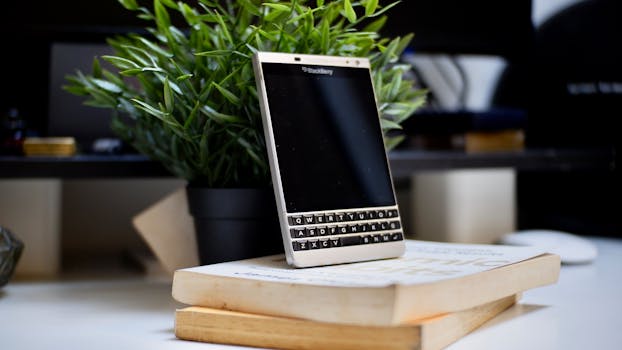 BlackBerry smartphone placed on books with a green plant background, showcasing a modern workspace.