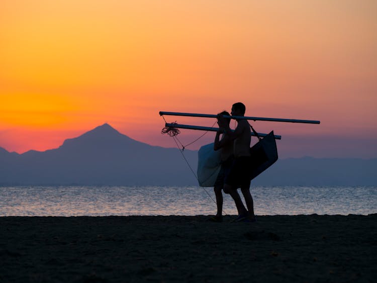 Person Carrying Pole While Walking Near Beach Shore