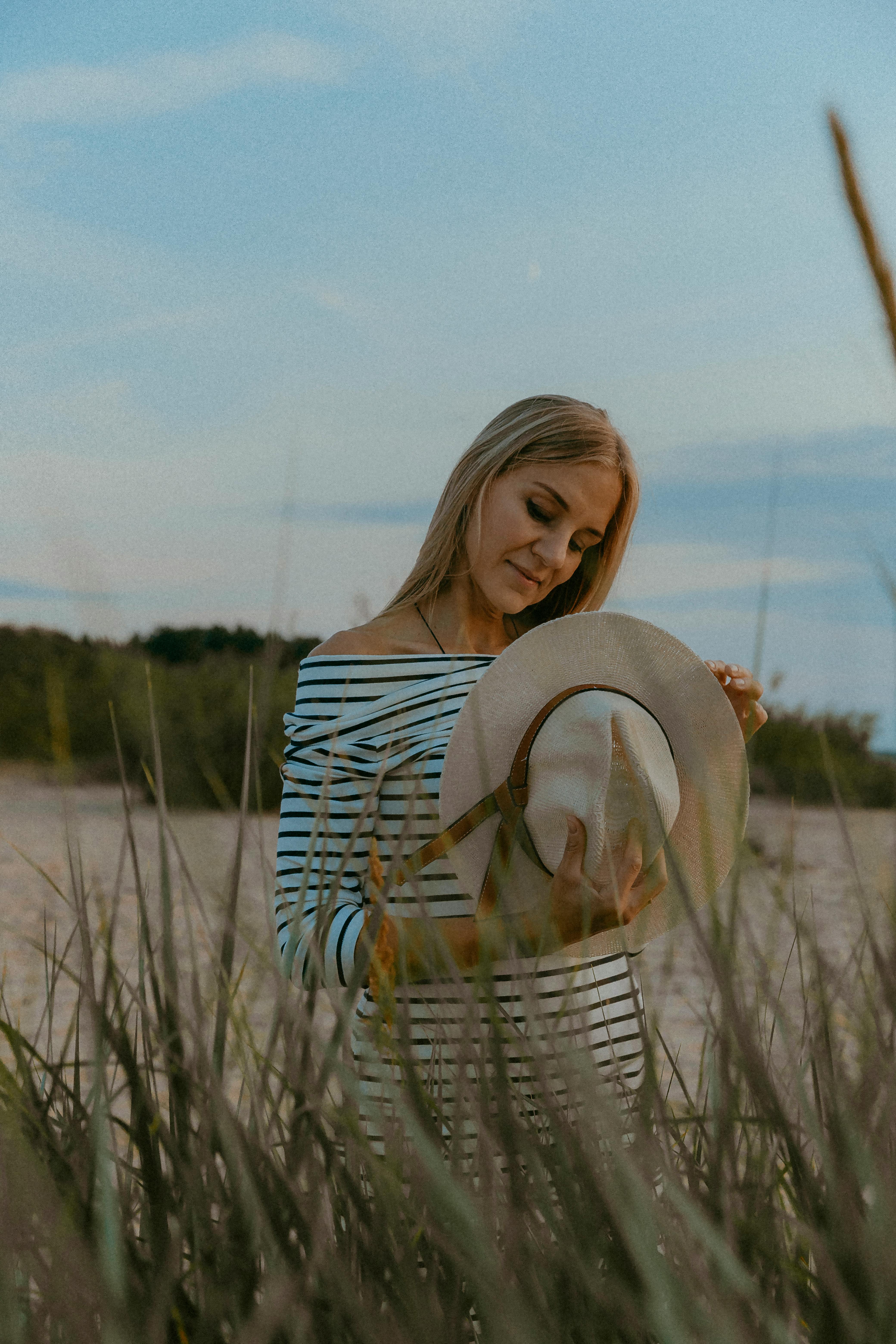 一名穿着条纹连衣裙的女子，在户外戴着草帽，若有所思地低头