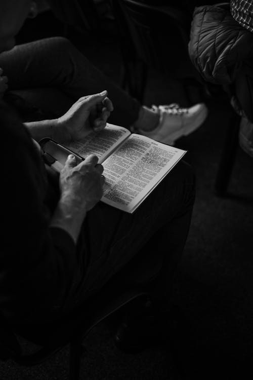 Black and White Photo of a Person Sitting Cross Legged with a Book 