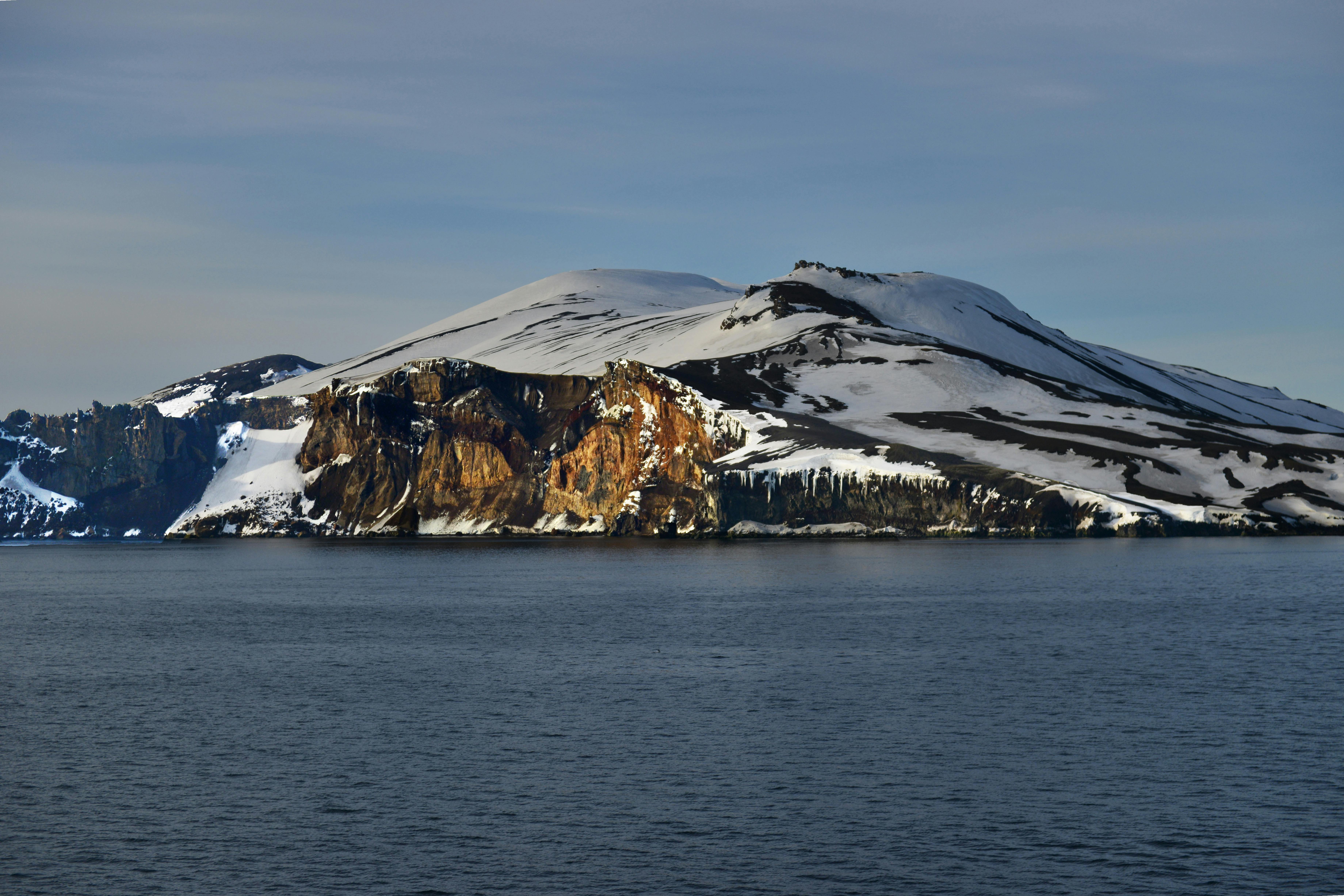 晴朗的天空下，白雪皑皑的岛屿景色宁静，平静的海水环绕着岩石悬崖