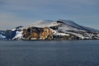晴朗的天空下，白雪皑皑的岛屿景色宁静，平静的海水环绕着岩石悬崖
