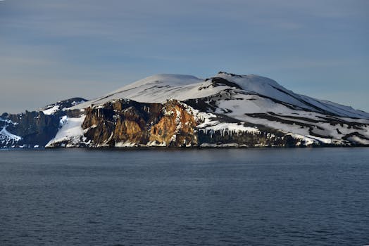 晴朗的天空下，白雪皑皑的岛屿景色宁静，平静的海水环绕着岩石悬崖