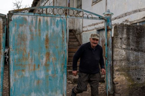 Free An elderly man in a village exiting through a weathered blue gate with a smile. Stock Photo