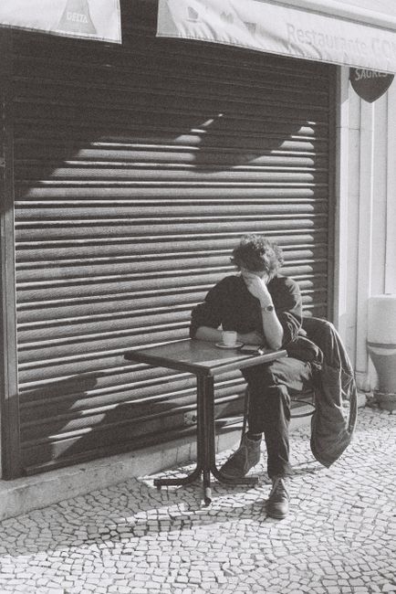 Monochrome shot of a man enjoying coffee outside a Lisbon cafe.