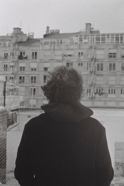 A person standing in front of a Lisbon apartment block in a black and white urban setting.