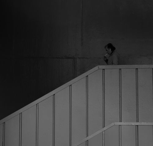 Free Black and white photo of a man smoking on a staircase, creating a moody urban scene. Stock Photo