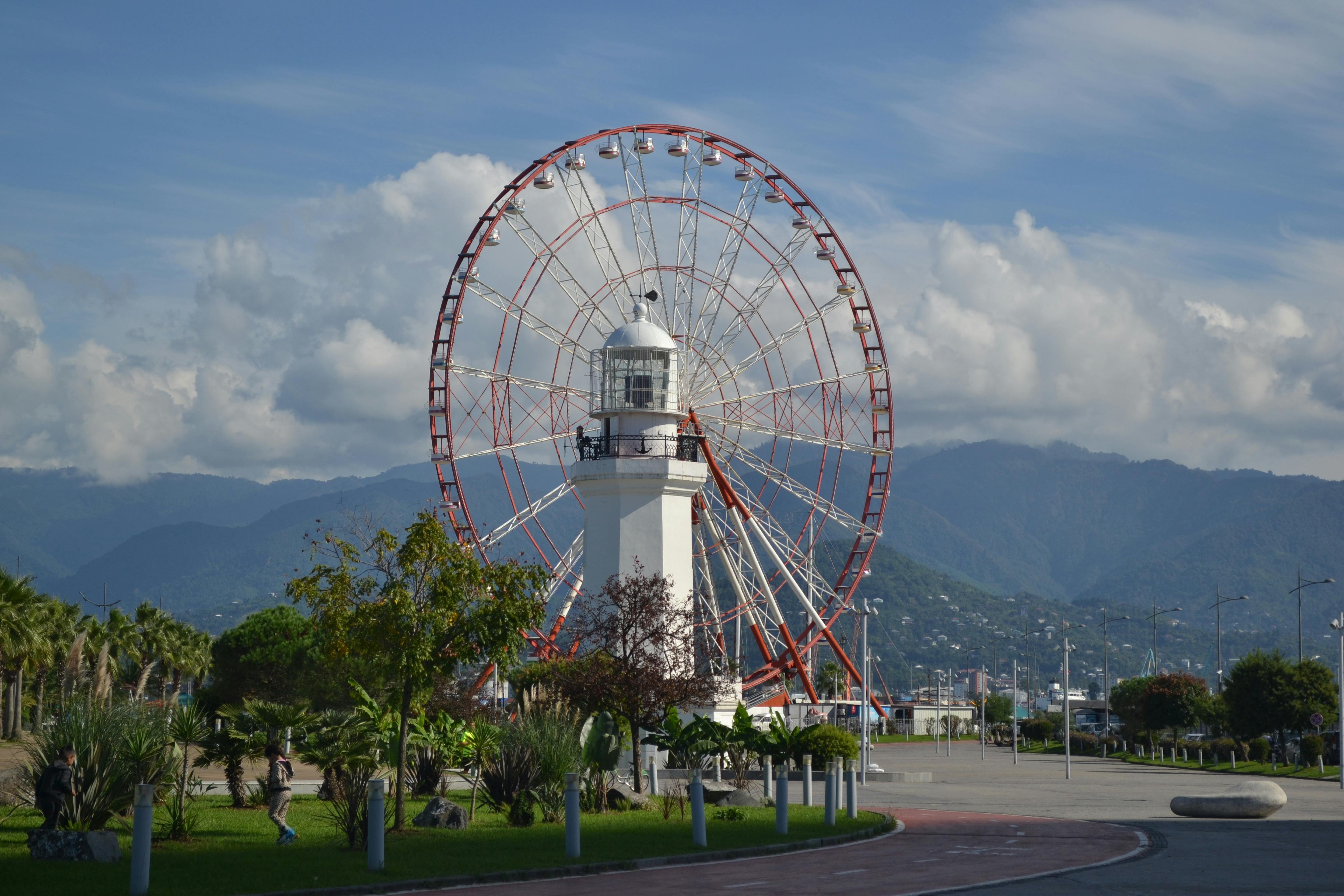 Stunning view of Batumi's iconic ferris wheel and lighthouse against mountainous backdrop.