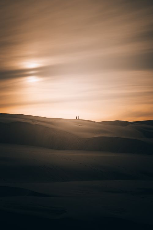 Free Serene desert landscape with silhouetted figures against a stunning sunset sky. Stock Photo