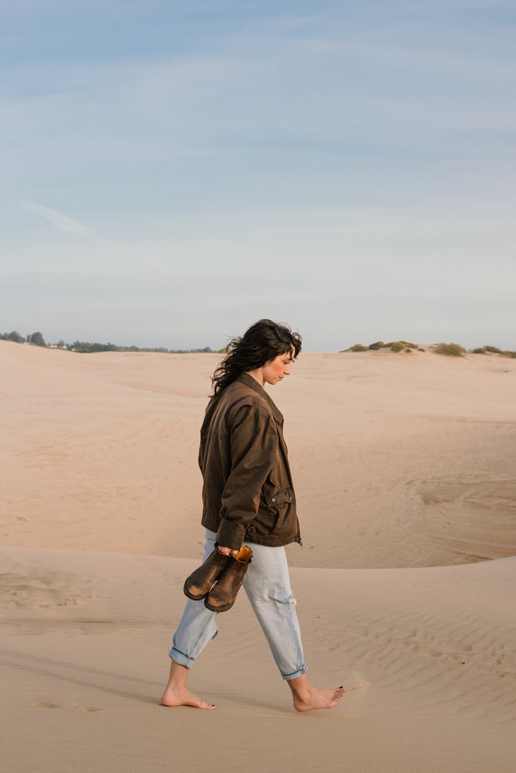 Woman Walking Through Sand Holding Shoes In Hand