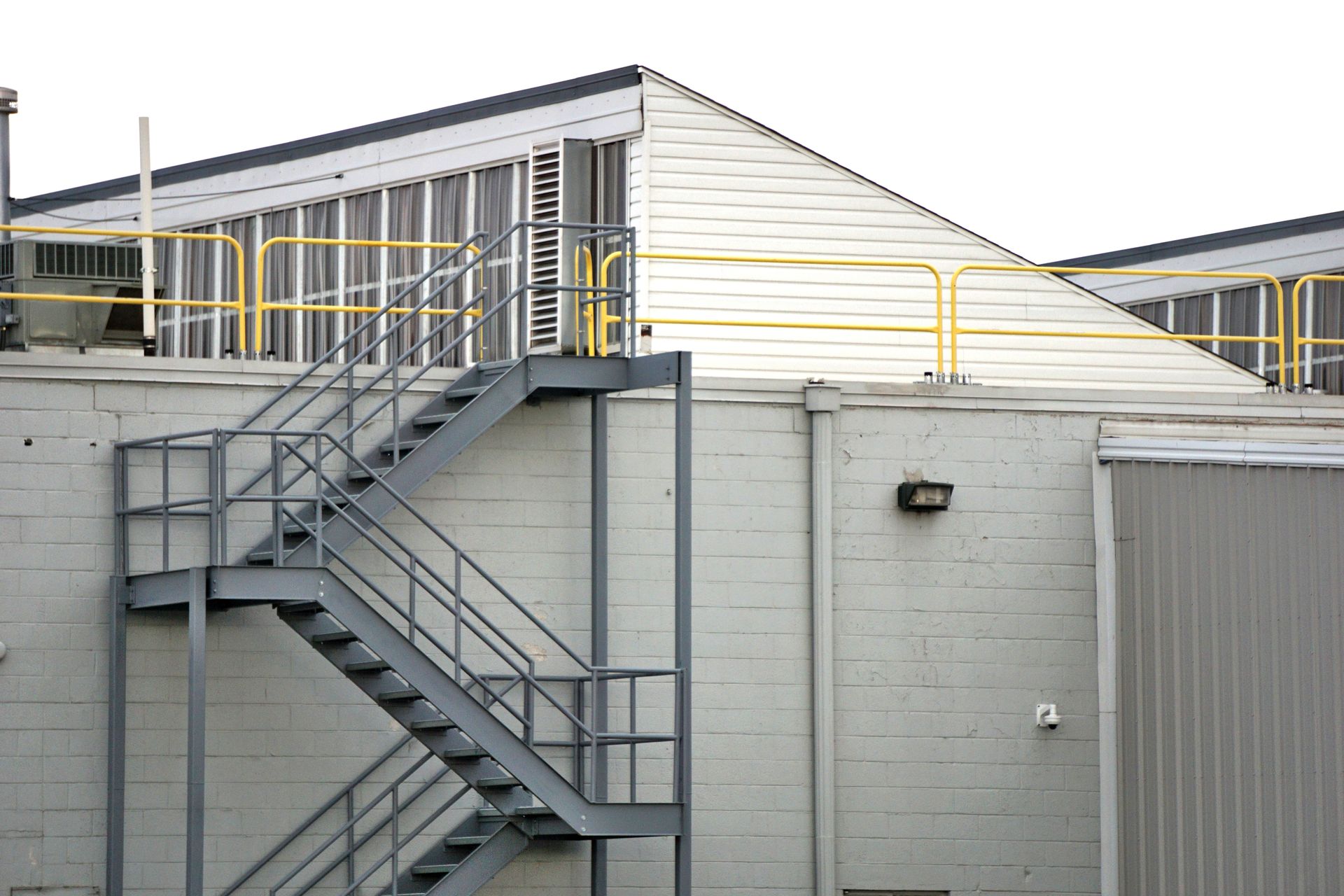 Exterior view of an industrial building with a prominent steel staircase and yellow railing.