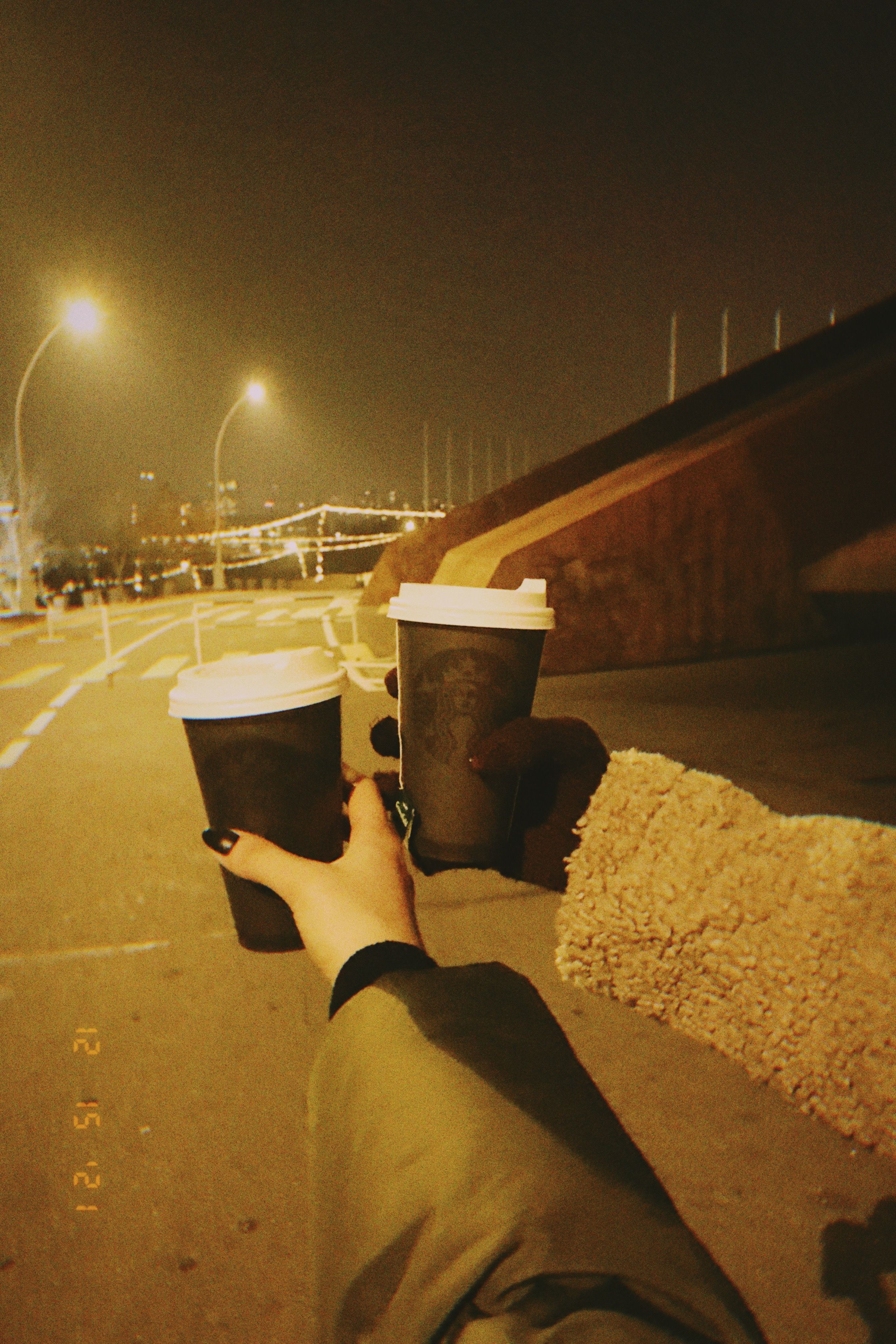Two hands holding coffee cups on a city street in Yerevan at night.