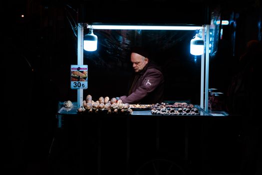 Elderly man selling roasted corn at a night market under neon lights. Urban street food scene.