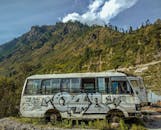 一辆涂鸦覆盖的废弃公交车，背靠风景优美的山地景观，映衬在蓝天下