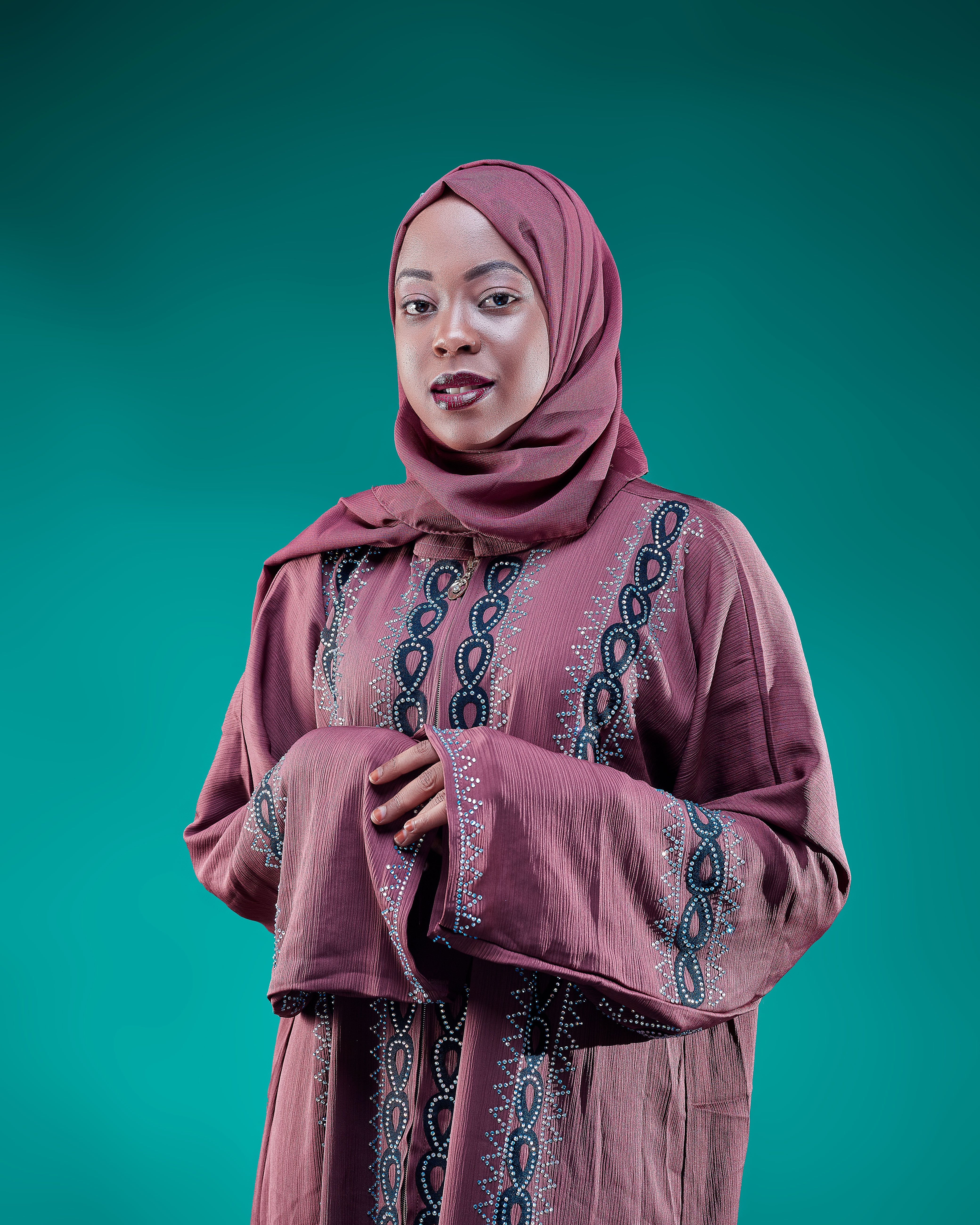Portrait of a young woman wearing a traditional hijab and elegant dress in a studio setting.