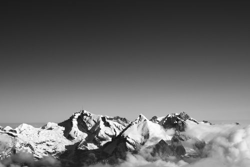 Free Dramatic aerial view of snow-covered mountain peaks emerging through clouds against a clear sky. Stock Photo
