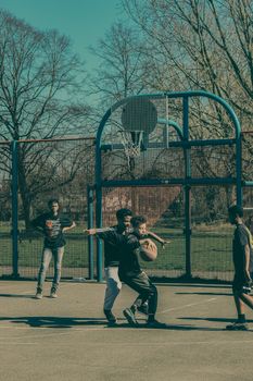 Group of teenagers playing basketball on an outdoor court on a sunny day.